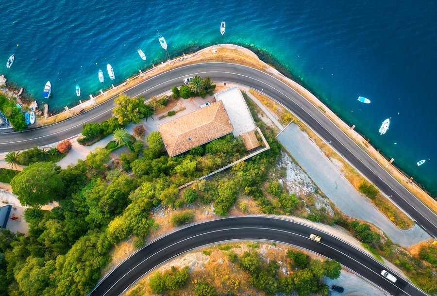 Aerial view of road, boats and yachts in water, buildings at sunset in spring. Colorful landscape with cars on roadway, sea coast, port, green trees in summer. Top view of highway in Croatia. Travel